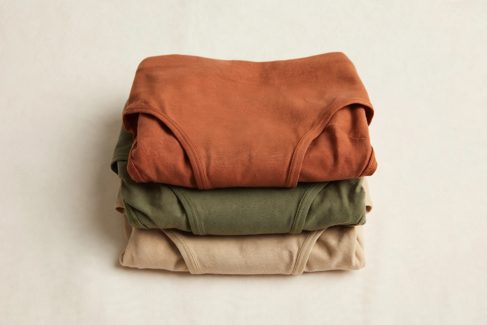 Neatly folded stack of women's cotton briefs in terracotta, olive and sand tones